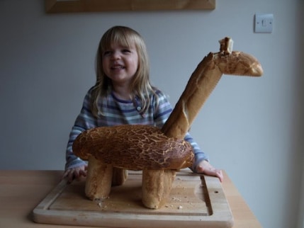 girl smiling behind a giraffe sculpture made of bread